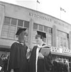Two Waterloo Lutheran University graduates in front of the Kitchener Memorial Auditorium