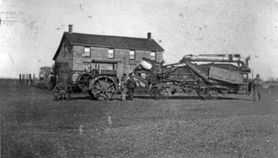 A combine harvester and tractor in front of the residence of Richard C. Pindar, c.1920-1925