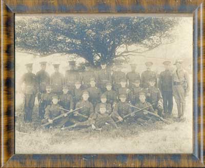 Group photo of 25 soldiers seated & standing under a tree