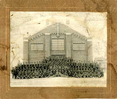 Group photograph of 6 rows of soldiers in front of a brick building