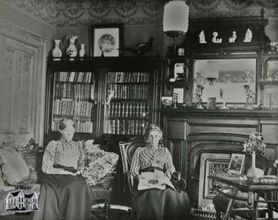 Mrs. Clench and Miss Cruttenden in the living room of the Clench home