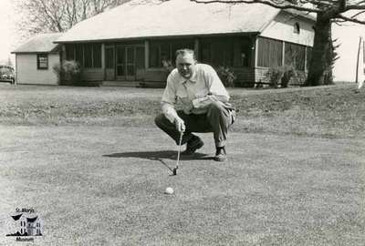 Golfer lining up a putt in front of the old golf course clubhouse