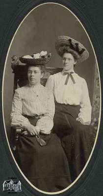 Two women seated; wearing straw hats