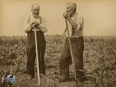 Two elderly men resting on hoes in field of young corn