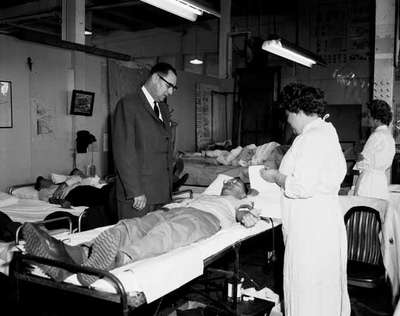 Omer Voss and a Female Nurse Look on as an Employee Donates Blood