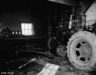 A man in his workshop with an IHC McCormick Farmall Super M tractor, and IHC McCormick Seed Drill.