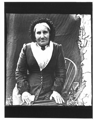 Portrait of a seated elderly woman in a black bonnet trimmed with ruffles.