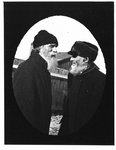 Outdoor portrait of two bearded gentleman in caps and overcoats.