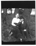 Portrait of a couple seated against a tree.