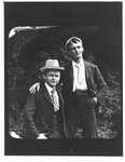 Outdoors portrait of two young men in suits and hats.