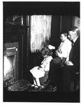 Portrait of John Connon with young boy and girl, seated by fireplace.