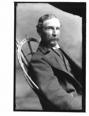 Portrait of a man seated in a rustic chair.