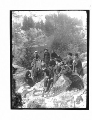 Group portrait of unidentified men and women on a rocky riverbank.