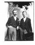 Portrait of 2 men, similarily dressed in black waistcoats, jackets and light trousers.