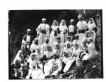 Group portrait of men and women in Arabian costumes, on a rocky river bank.