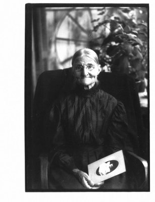 Portrait of an unidentified elderly woman holding a photograph of a child.