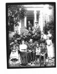 Group portrait of unidentified men, women and children in front of a house.