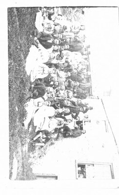 Group portrait of unidentified men and women beside a stone house.