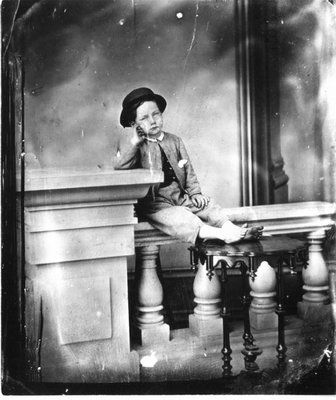 Studio portrait of an unidentified young boy sitting on a railing.