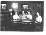 Portrait of an unidentified man, woman, and two children seated around a library table, Connon photographs are on the wall.