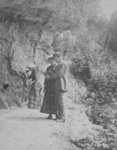 A man and woman look at an open book, while another woman drinks from a spring in the Elora rocks.