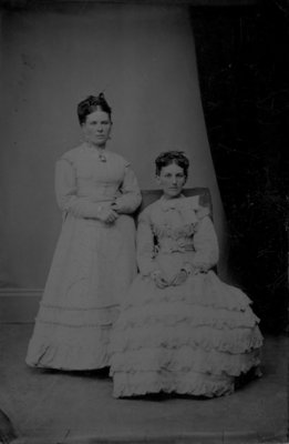 Full length portrait of two women in light dresses.