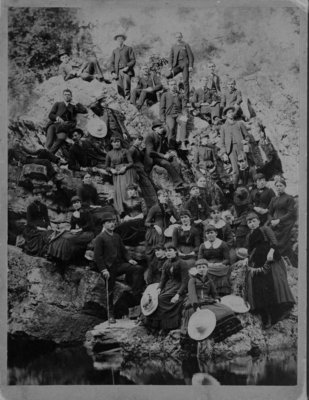 Large group of men and women posed on rocky river bank.