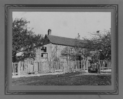 A board and batten house with missing window panes, picket fence and gate.