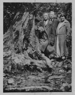 Portrait of John Connon with an unidentified man and woman, standing beside a tree stump.