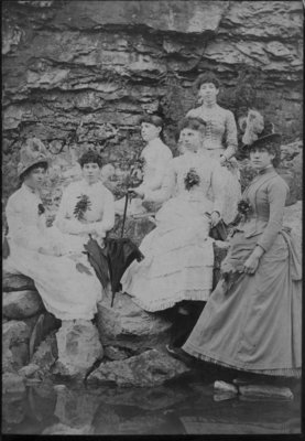 Group portrait of six unidentified young women, posed on a rocky river bank.