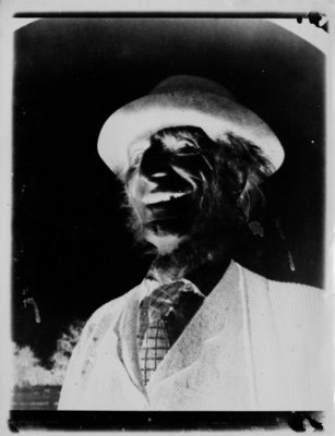 Negative print of bust portrait of laughing man wearing a hat with rolled brim.