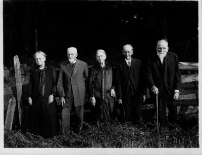 Group portrait of 5 elderly people [3 men, 2 women], in front of a fence.