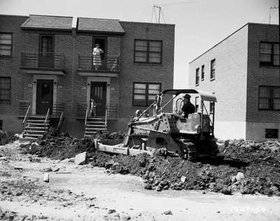 Man on Tractor Excavating Dirt as Woman and Child Watch