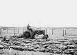 Man Ploughing [Plowing] a Field With Town in the Background