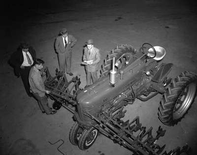 Three Men in Suits Look on as Another Shows Them a Tractor