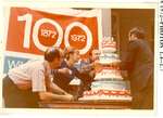 Three people adding layers to the Centennial cake